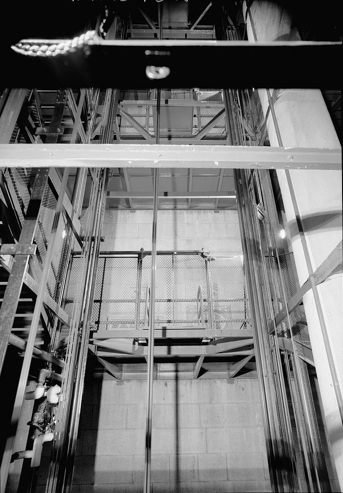 Black-and-white photographs showing the inside of the Washington Monument’s elevator shaft. The images reveal metal beams, rails, and a fenced platform that makes up part of the elevator system. The elevator cage is visible in some shots, as are cables and machinery used to operate the system. The photographs highlight the industrial complexity and vertical expanse of the monument’s inner structure.