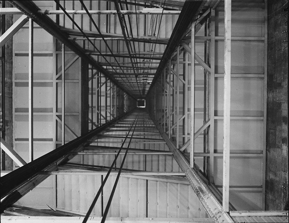 Black-and-white photographs showing the interior of the Washington Monument’s elevator shaft, captured from the bottom and looking straight up. The images reveal the steel and wood framing structure, creating a tunnel-like perspective that narrows into a small bright opening at the top. The detailed construction shows the complex network of beams, crossbars, and supports inside the monument.