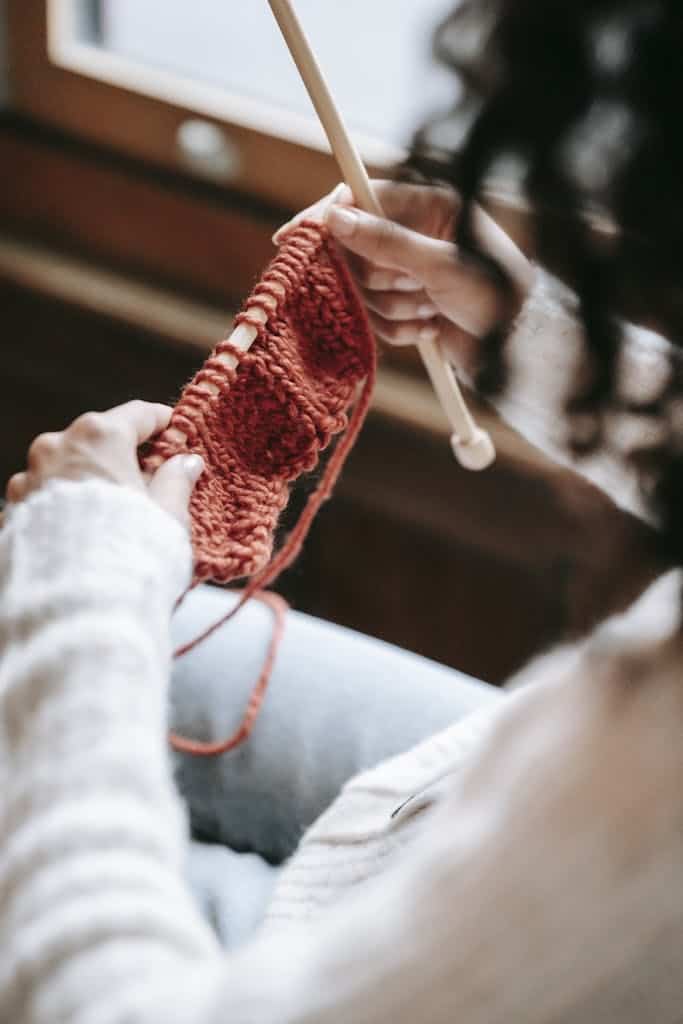 A woman knitting a cozy orange scarf with wool yarn indoors.