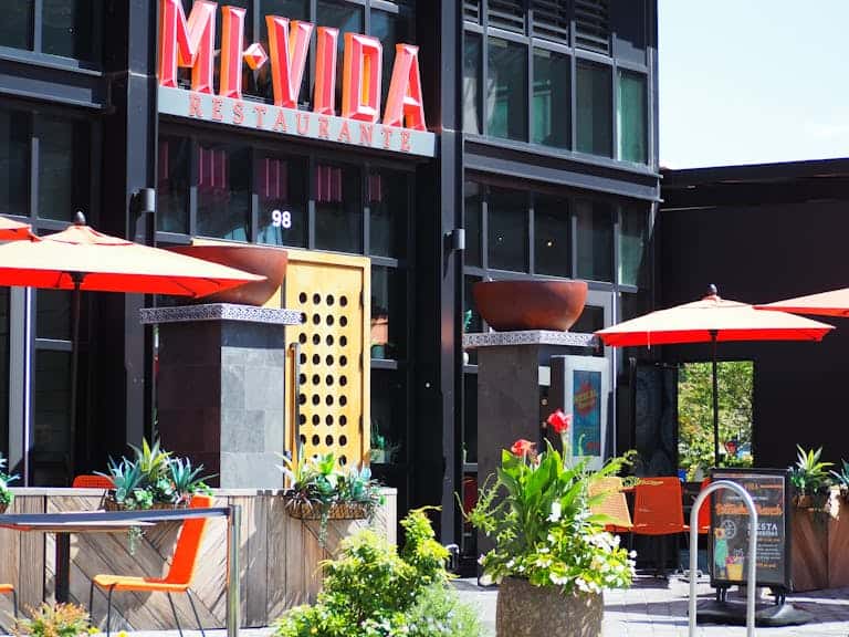 Colorful outdoor seating at Mi Vida Restaurant in Washington, DC, with red umbrellas and lush plants.