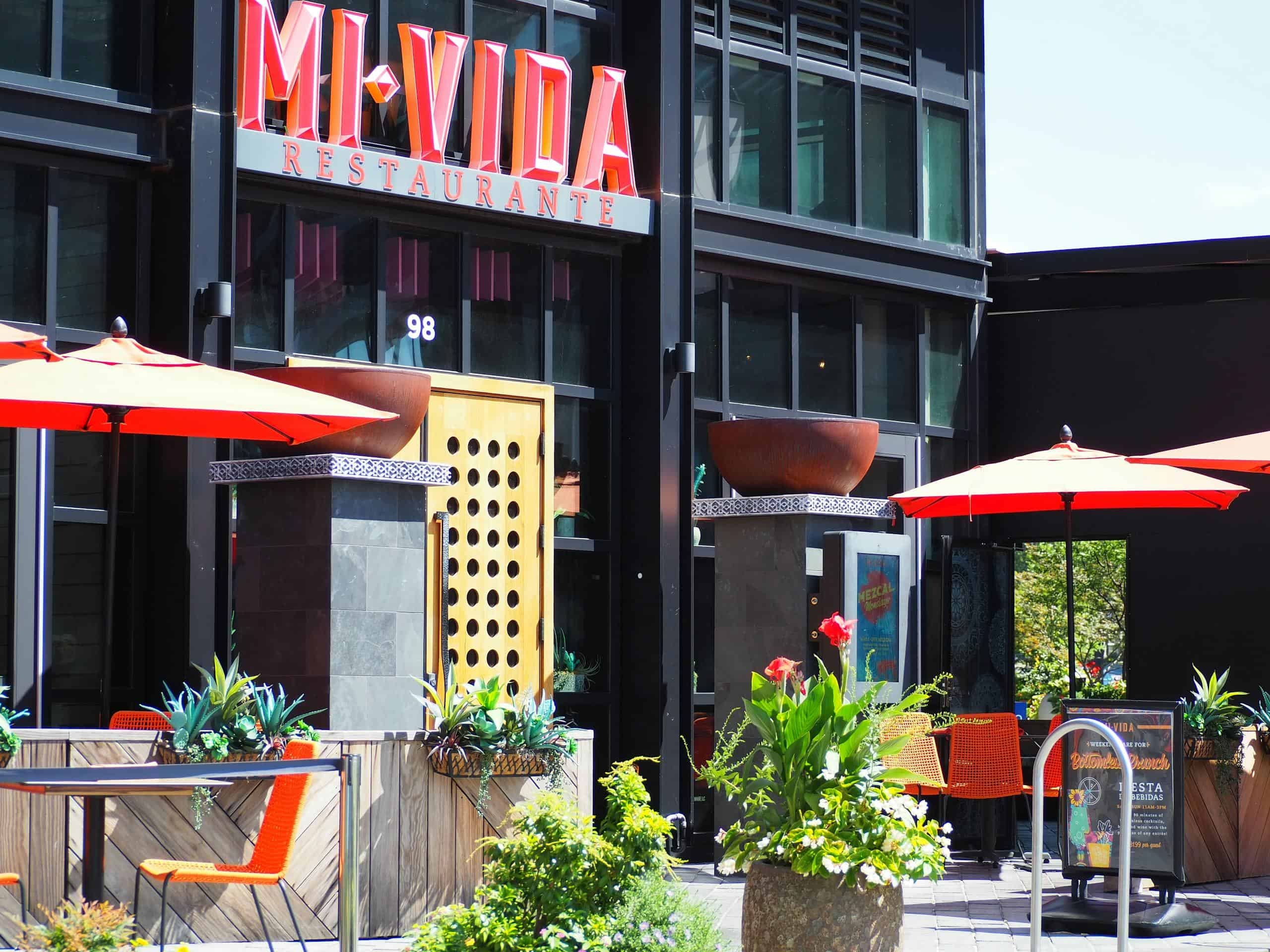 Colorful outdoor seating at Mi Vida Restaurant in Washington, DC, with red umbrellas and lush plants.